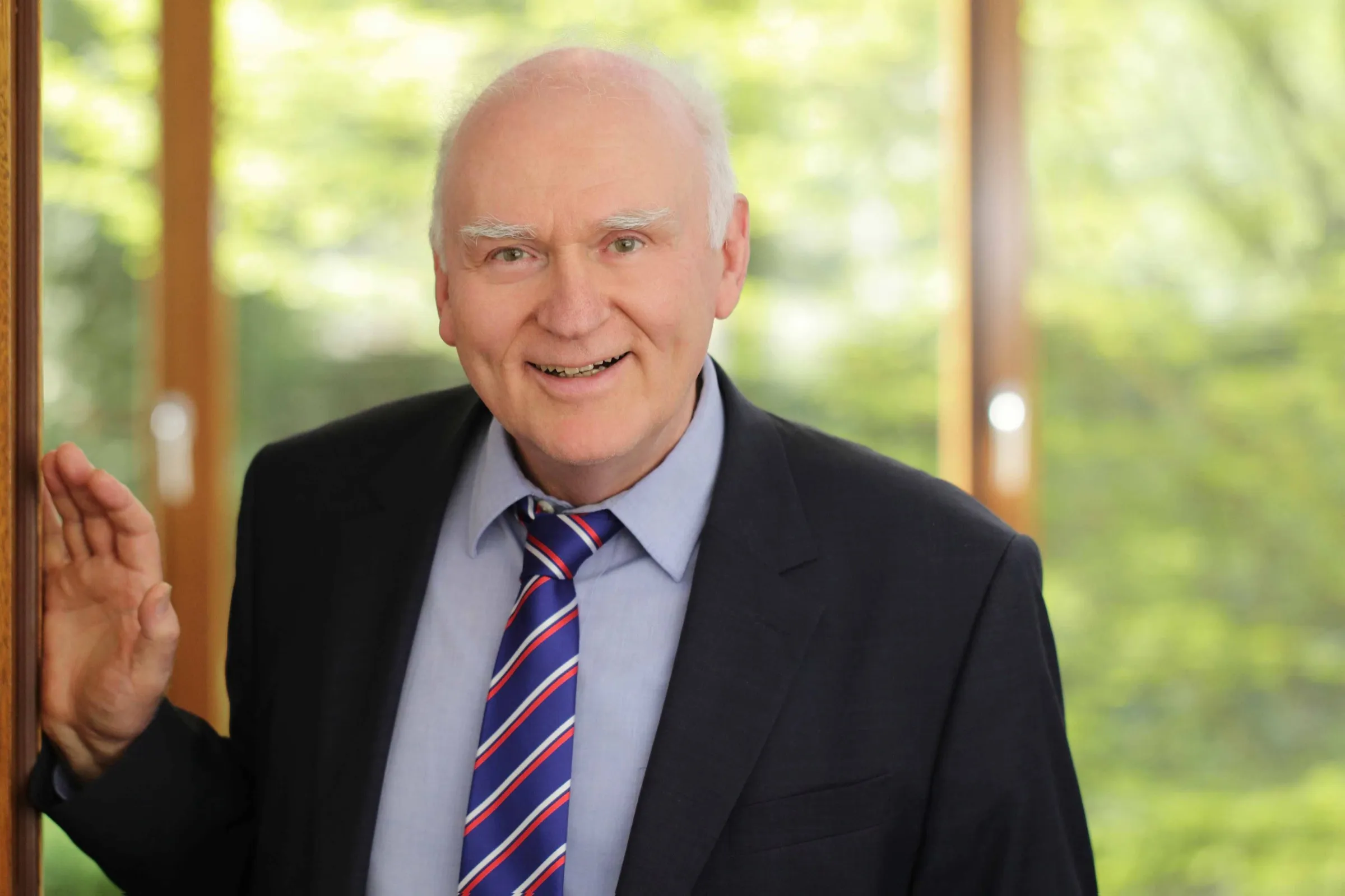 Prof. Dr. Rainer Thome lächelnd vor einem Fenster mit Blick ins Grüne